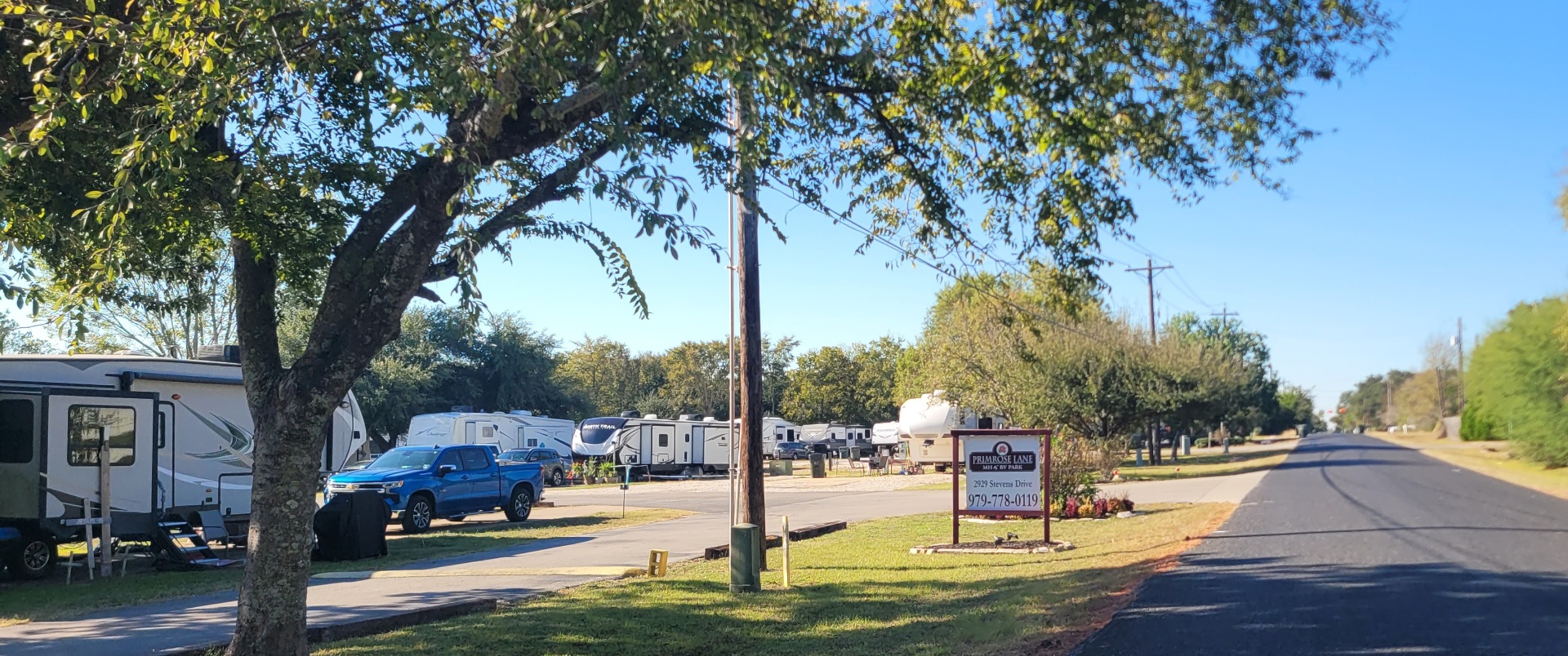 Primrose Lane RV Park entrance sign on Stevens Drive with rows of RVs under shade trees